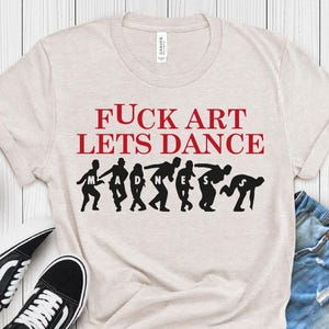May include: A light grey t-shirt with the text "FUCK ART LETS DANCE" in red, and a black graphic of dancing figures. The shirt is paired with denim shorts and black and white trainers. The bottom left corner has a black rectangle with the text "H. COOL GREY".