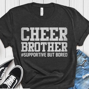Op de afbeelding: Donkergrijs T-shirt met witte tekst die "Cheer Brother #Supportive But Bored" zegt.