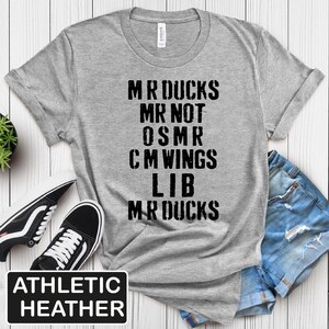 May include: Athletic heather gray t-shirt with the text "MR DUCKS MR NOT OSMR CM WINGS LIB MR DUCKS" in black. The shirt is paired with black and white sneakers and denim shorts.