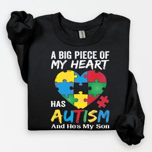 May include: Black t-shirt with a colorful puzzle piece heart and the text "A big piece of my heart has autism and he's my son".
