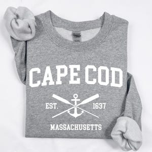 Puede incluir: Sudadera gris con texto blanco que dice "CAPE COD EST. 1637 MASSACHUSETTS" con un diseño de ancla y remos blancos.