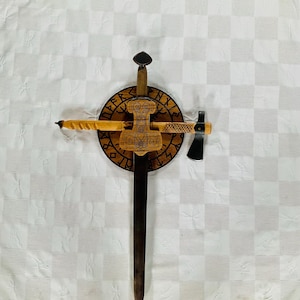 May include: A wooden display featuring a sword, a small axe, and a wooden shield with carved runes and a Thor's hammer design. The sword has a dark blade and a wooden handle. The axe has a black head and a wooden handle. The shield is circular.