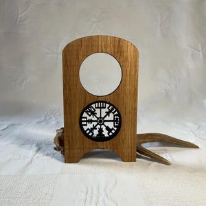 Op de afbeelding: Houten standaard met een ronde uitsparing en een zwart Vegvisir-symbool. De standaard is gemaakt van lichtbruin hout en heeft een rustieke uitstraling.