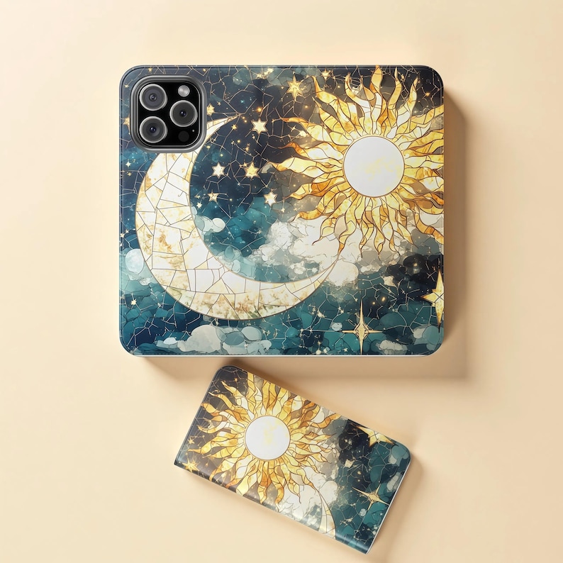 Op de afbeelding: Een telefoonhoesje en een kleiner accessoire met een hemels ontwerp. Het ontwerp bevat een maan, een stralende zon, sterren en wolken tegen een donkerblauwe en blauwgroene achtergrond. De zon en maan hebben een glas-in-lood effect.