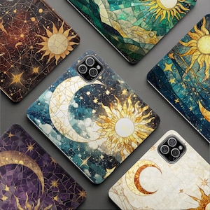 Puede incluir: Una colección de fundas para teléfonos con diseños celestiales. Cada funda presenta una ilustración de estilo vidriera del sol, la luna y las estrellas en varias paletas de colores, incluyendo azules, dorados y morados. Las fundas están dispuestas sobre una superficie gris.