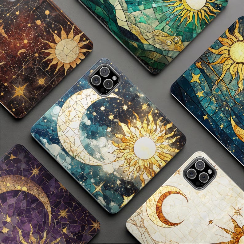 Op de afbeelding: Een verzameling telefoonhoesjes met hemelse ontwerpen. Elke hoes heeft een illustratie in glas-in-loodstijl van de zon, maan en sterren in verschillende kleurenpaletten, waaronder blauw, goud en paars. De hoesjes zijn gerangschikt op een grijze ondergrond.