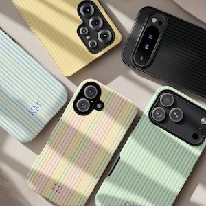 May include: An assortment of colorful phone cases with striped patterns. The cases are in various colors, including yellow, blue, green, and a multi-colored pastel design. Some cases have initials printed on them. The cases are designed for different phone models.