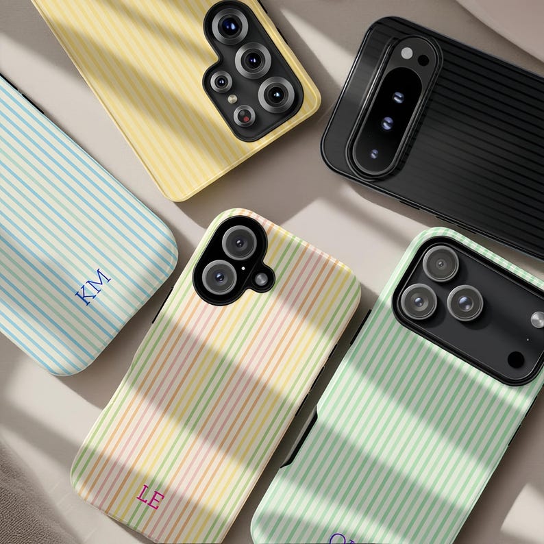May include: An assortment of colorful phone cases with striped patterns. The cases are in various colors, including yellow, blue, green, and a multi-colored pastel design. Some cases have initials printed on them. The cases are designed for different phone models.