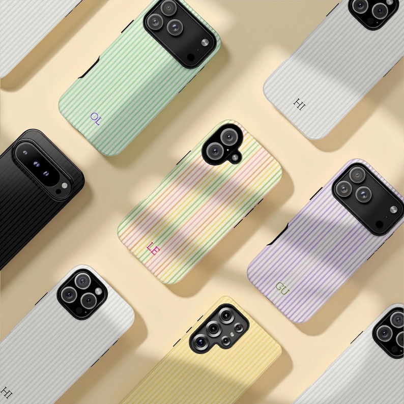 May include: A collection of smartphone cases with a striped pattern in various pastel colors, including green, yellow, and purple. Each case has a different initial printed on it. The cases are arranged on a light beige surface.