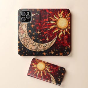 Op de afbeelding: Een telefoonhoesje en een telefoonhouder met een glas-in-lood ontwerp van een zon, maan en sterren in rood, goud en cr&egrave;me tinten. De telefoonhoes heeft een zwarte rand en een camera-uitsparing. De telefoonhouder heeft een bijpassend ontwerp.