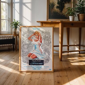 May include: A framed vintage movie poster featuring Brigitte Bardot in a light blue dress. The poster has a light wood frame and is displayed on a wooden floor. The poster's title is "Parisienne".