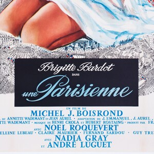 May include: A vintage movie poster for "Une Parisienne" featuring Brigitte Bardot. The poster has a black background with white and blue text, including the film title and credits. The top of the poster shows a partial illustration of a woman and a cityscape.