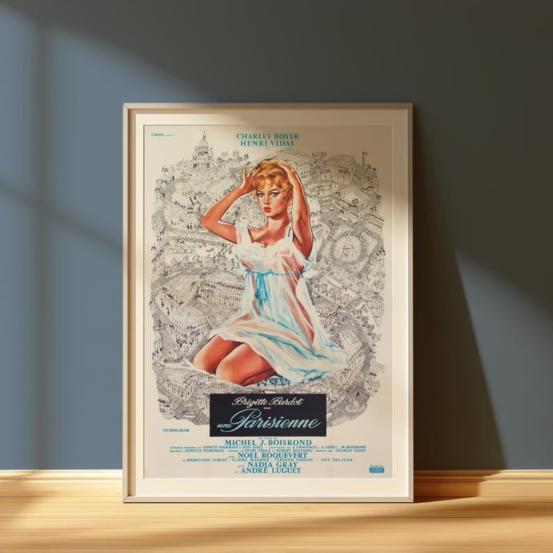May include: Framed vintage movie poster for "Une Parisienne" featuring Brigitte Bardot. The poster has a light background with a black and white illustration of Paris. The poster has a woman in a white dress with a blue ribbon.
