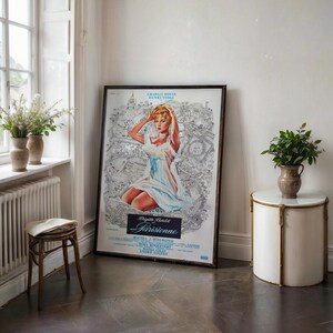 May include: A framed vintage movie poster featuring a woman in a white dress, with the title "Parisienne". The poster is leaning against a white wall. A small, round side table with a marble top and a vase of greenery are next to the poster.