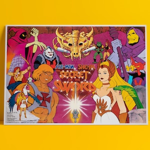 May include: A vintage poster for "He-Man and She-Ra: The Secret of the Sword" features cartoon characters in vibrant colors. The poster includes He-Man, She-Ra, Skeletor, and other characters, with the title prominently displayed.