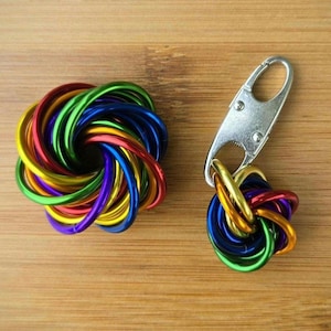 May include: A colorful, handmade keychain and a matching decorative item. The items are made of intertwined metal rings in a rainbow of colors, including red, orange, yellow, green, blue, and purple. The keychain has a silver clasp.