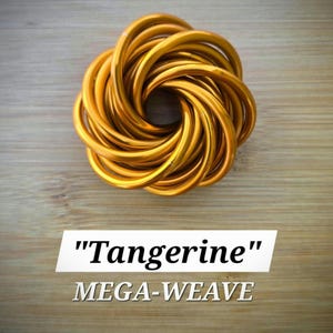 May include: A golden-orange, circular sculpture made of intertwined, curved metal tubes. The sculpture is centered on a light brown wooden surface. The text "Tangerine" and "MEGA-WEAVE" are displayed in white text below the sculpture.
