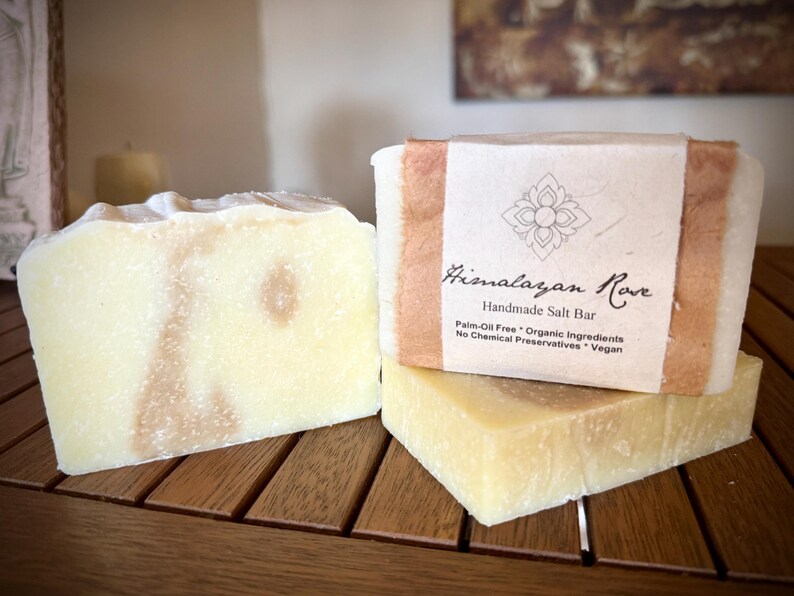 Op de afbeelding: Twee repen handgemaakte Himalayazoutzeep van Himalayan Rove. De zeep is lichtgeel met bruine swirls. De bovenste reep heeft een bruin papieren etiket met de tekst "Himalayan Rove Handgemaakte Zoutzeep Palmolievrij * Biologische Ingredi&euml;nten Geen Chemische Conserveermiddelen * Vegan".