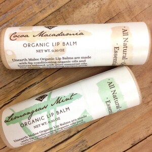 May include: Two tubes of organic lip balm, one with a cocoa macadamia scent and the other with a lemongrass mint scent. Both tubes are labelled "All Natural" and "Essential Oils" and have a net weight of 0.30 oz.