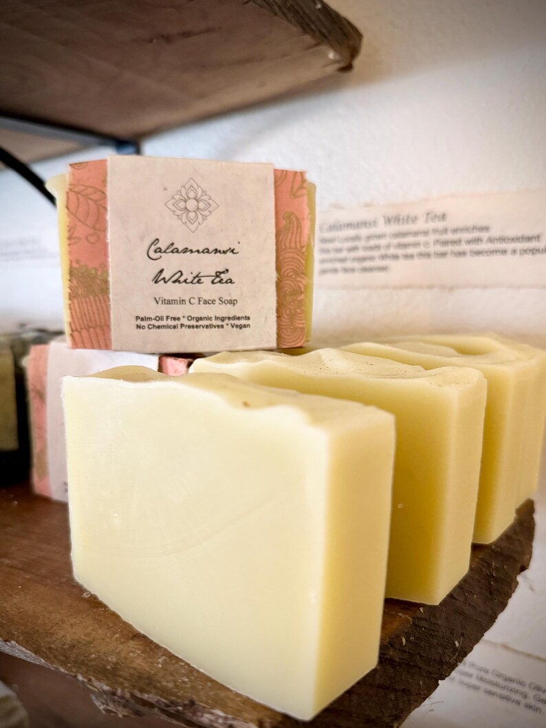 May include: Four bars of white soap with a pink and gold label that reads "Calamansi White Tea Vitamin C Face Soap Palm-Oil Free * Organic Ingredients No Chemical Preservatives * Vegan"