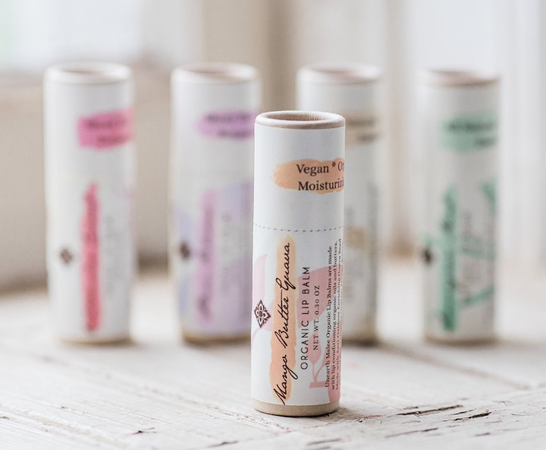 Puede incluir: Un primer plano de un tubo de b&aacute;lsamo labial org&aacute;nico con sabor a mango y guayaba. El tubo est&aacute; hecho de cart&oacute;n y tiene una etiqueta blanca con texto marr&oacute;n. El texto de la etiqueta dice "Manga Buttee Guava Organic Lip Balm Net Wt. 0.30 oz Vegan * Organic Moisturizer".