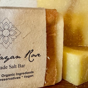 Op de afbeelding: Een handgemaakte Himalaya-zoutstaaf, verpakt in bruin papier met een label waarop staat "Himalayan Rove Handmade Salt Bar Palm-Oil Free * Organic Ingredients No Chemical Preservatives * Vegan".