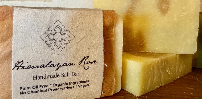 Op de afbeelding: Een handgemaakte Himalaya-zoutstaaf, verpakt in bruin papier met een label waarop staat "Himalayan Rove Handmade Salt Bar Palm-Oil Free * Organic Ingredients No Chemical Preservatives * Vegan".