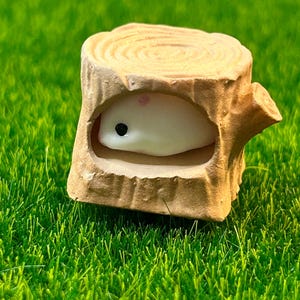 May include: A small white ceramic figurine of a hamster inside a brown ceramic tree stump. The stump has a hollowed-out space for the hamster to fit inside.