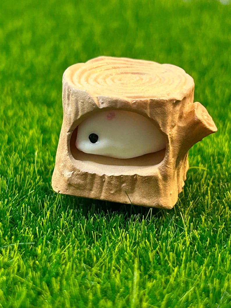 May include: A small white ceramic figurine of a hamster inside a brown ceramic tree stump. The stump has a hollowed-out space for the hamster to fit inside.