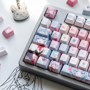 Può includere: Una tastiera meccanica grigia con tasti personalizzati con illustrazioni in stile anime dai colori pastello. I tasti presentano vari disegni, tra cui personaggi anime, cuori e motivi a coniglietto. Sono visibili anche un portachiavi a coniglietto e tasti extra.