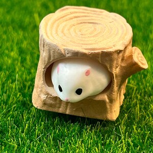 May include: A white ceramic hamster figurine peeking out of a brown ceramic tree stump. The stump has a circular top with concentric rings.