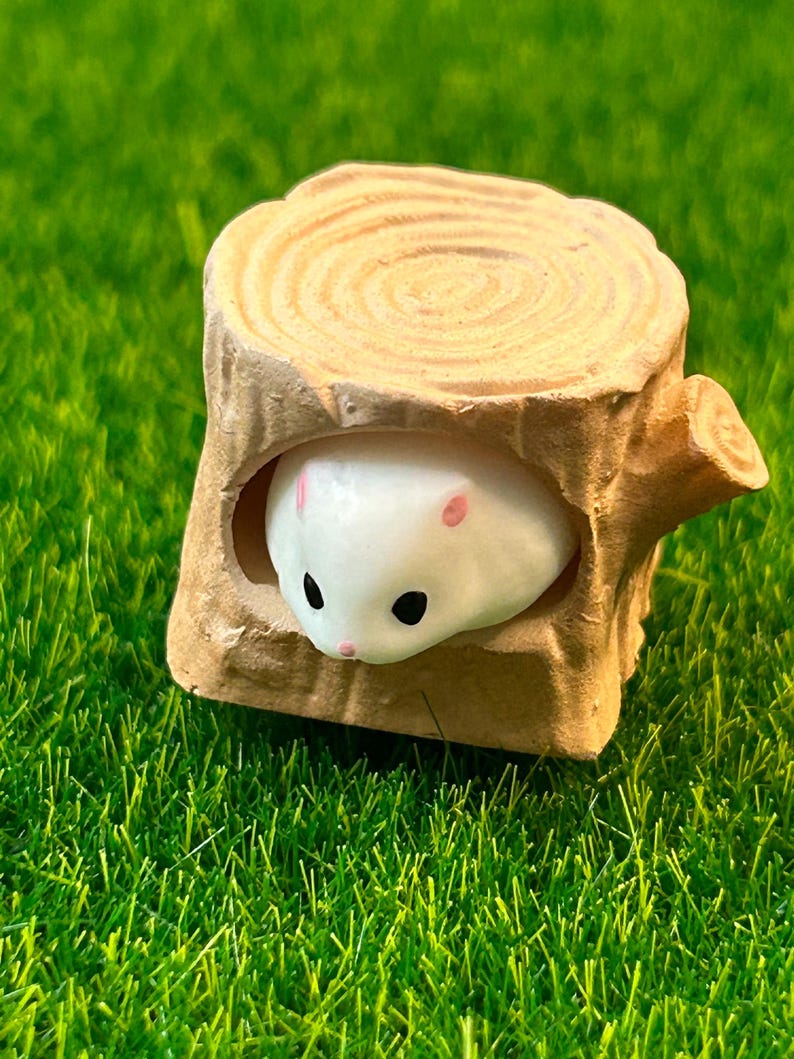 May include: A white ceramic hamster figurine peeking out of a brown ceramic tree stump. The stump has a circular top with concentric rings.