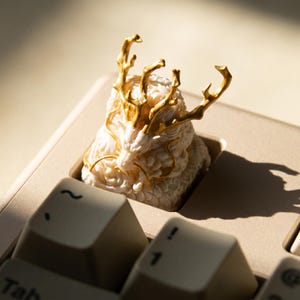 以下が含まれることがあります： ベージュ色のキーボードに配置された、金色のアクセントが付いた象牙色のドラゴンのキーキャップ。 ドラゴンの頭と角は精巧に彫刻されており、ユニークなキーボードアクセサリーを作成しています。 キーキャップは標準のキーを置き換えます。