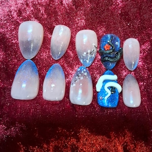 Könnte beinhalten: Ein Set aus zehn künstlichen Nägeln mit verschiedenen Designs. Einige Nägel weisen einen Farbverlauf auf, der von Rosa zu Blau übergeht. Andere zeigen florale Muster oder eine blaue Basis mit einem Schlangen- und Blumenmuster. Die Nägel sind oval geformt.