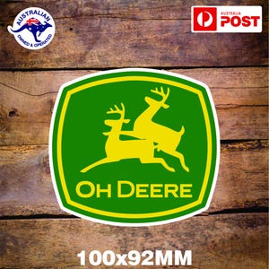 Könnte beinhalten: Grüner und gelber Aufkleber mit zwei Rehen, die übereinander springen. Der Text "OH DEERE" ist in gelben Buchstaben auf dem Aufkleber geschrieben. Der Aufkleber ist 100x92mm groß.