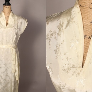 May include: A white satin dress with a floral pattern and a mandarin collar. The dress has a sash tie at the waist and short sleeves.