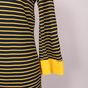Puede incluir: Un vestido de manga larga con rayas amarillas y azul marino. El vestido tiene una manga acampanada y un pu&ntilde;o amarillo.