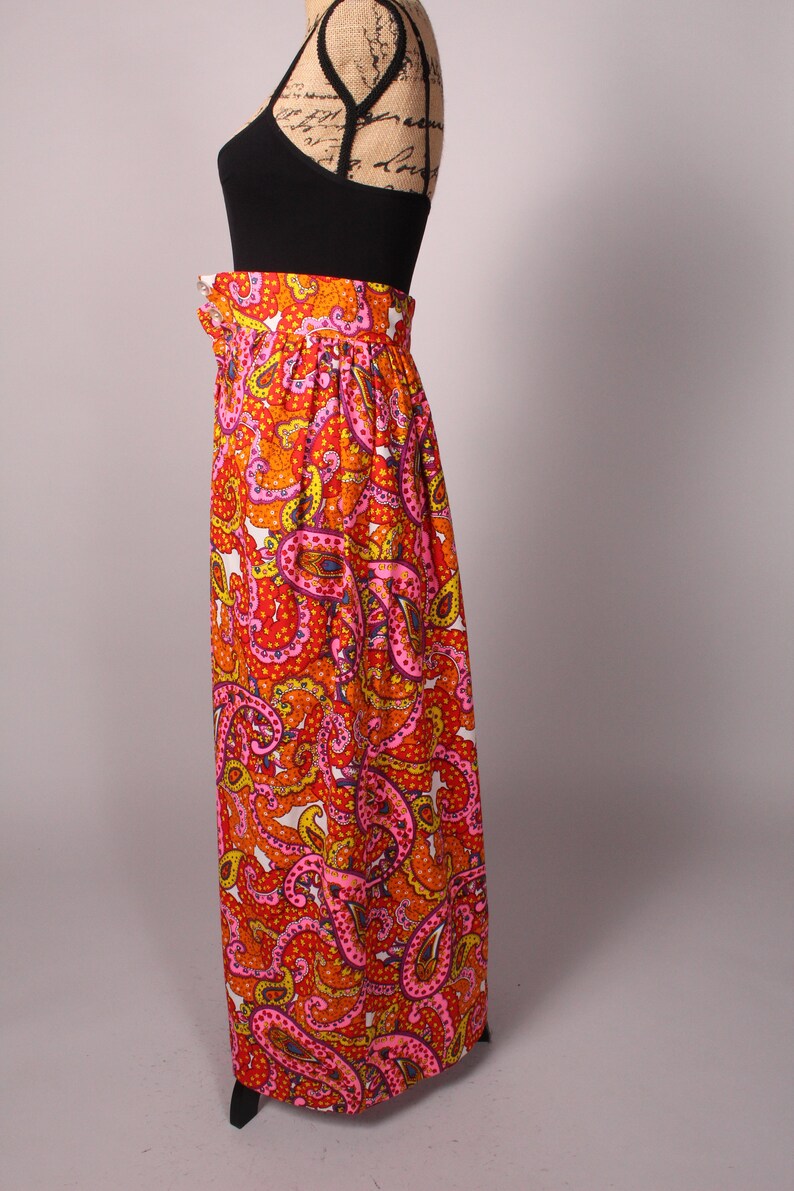 May include: A long, flowing skirt with a paisley print in shades of orange, pink, and yellow. The skirt has a high waist and a gathered design.
