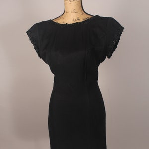 May include: A black sleeveless dress with a scoop neck and lace trim on the neckline and sleeves. The dress is fitted and has a short length.