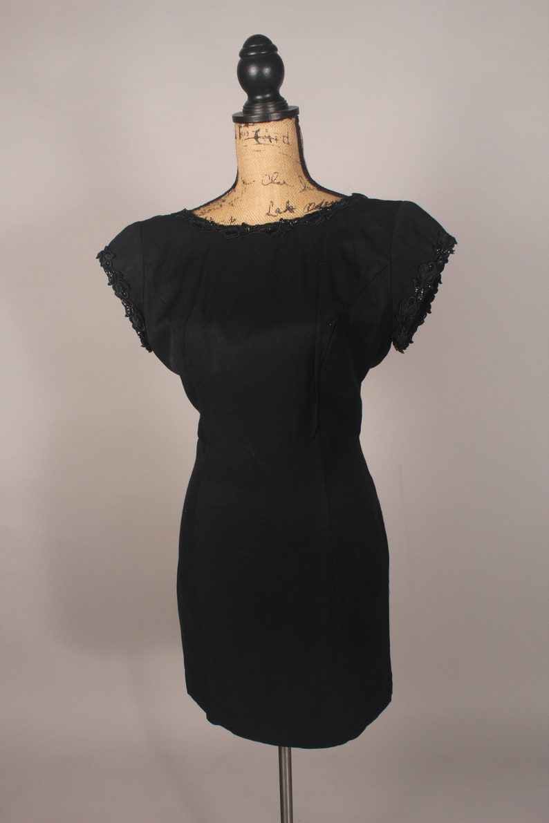 May include: A black sleeveless dress with a scoop neck and lace trim on the neckline and sleeves. The dress is fitted and has a short length.