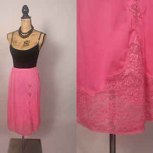 May include: A pink satin slip skirt with a lace trim. The skirt is knee-length and has a straight silhouette.