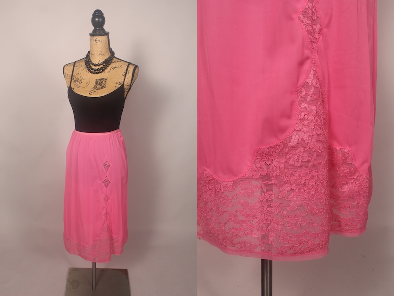 May include: A pink satin slip skirt with a lace trim. The skirt is knee-length and has a straight silhouette.