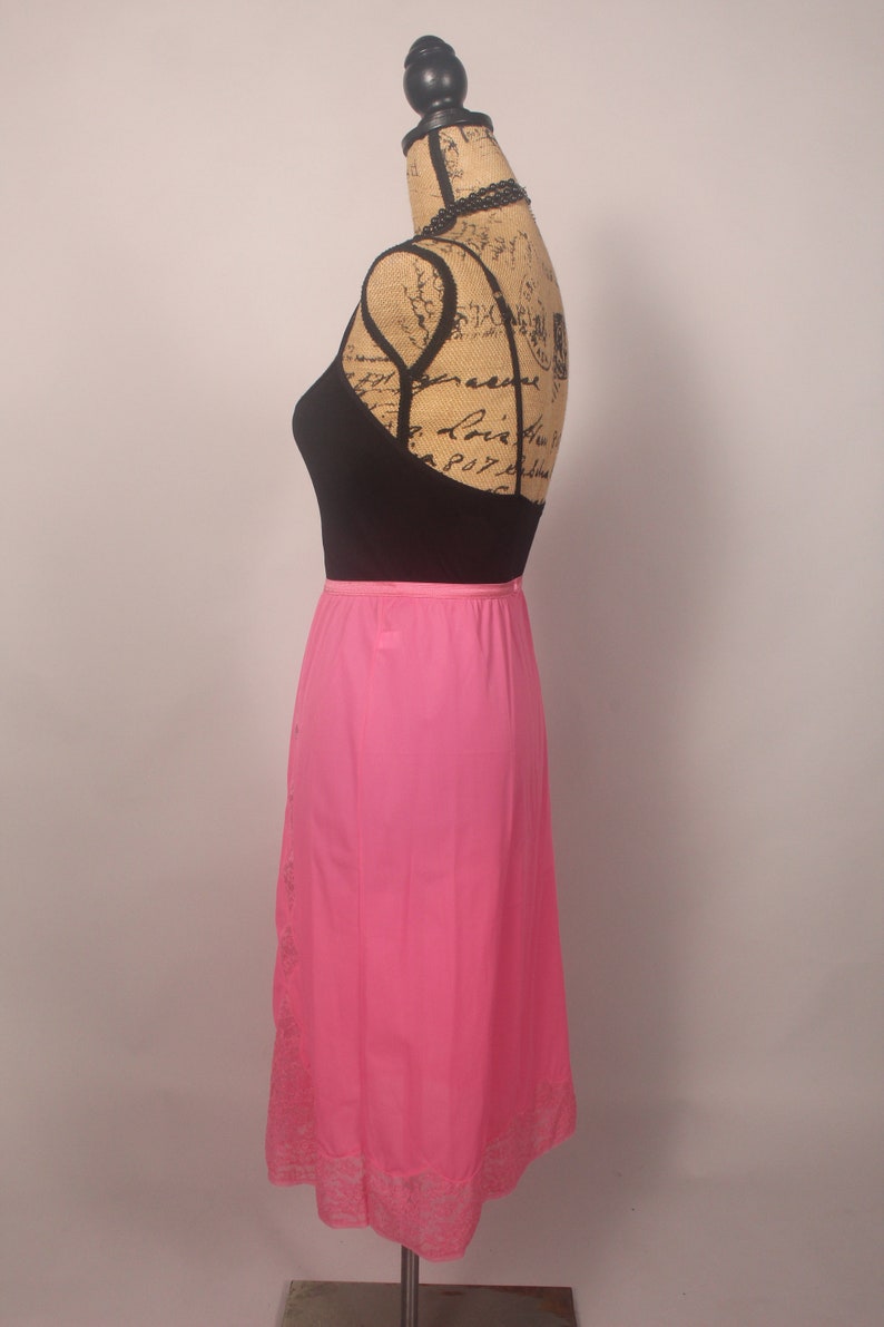 May include: A pink slip skirt with a lace trim. The skirt is on a mannequin and is made of a silky material.