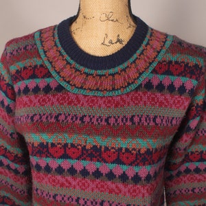 Puede incluir: Un su&eacute;ter de punto multicolor con un patr&oacute;n de punto de trenza. El su&eacute;ter tiene un cuello redondo azul marino y est&aacute; hecho de un material suave y c&aacute;lido.