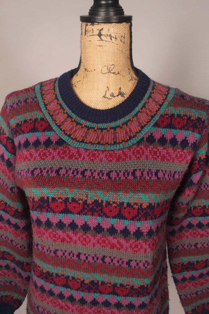 Puede incluir: Un su&eacute;ter de punto multicolor con un patr&oacute;n de punto de trenza. El su&eacute;ter tiene un cuello redondo azul marino y est&aacute; hecho de un material suave y c&aacute;lido.