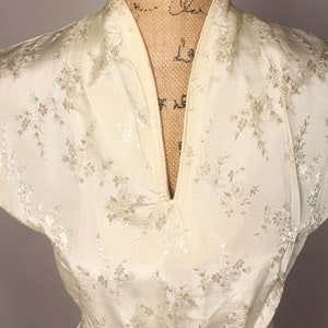 May include: A white satin dress with a floral pattern and a V-neckline. The dress has short sleeves and a sash.