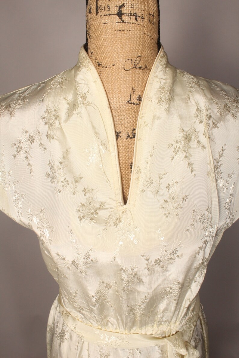 May include: A white satin dress with a floral pattern and a V-neckline. The dress has short sleeves and a sash.