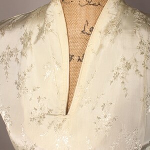 May include: Close-up of the neckline of a white satin dress with a floral pattern. The dress has a V-neck and a mandarin collar.