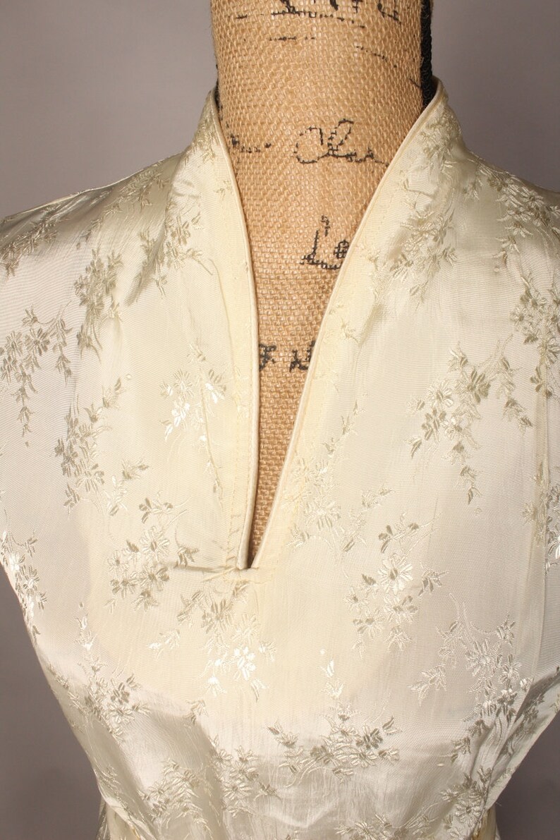 May include: Close-up of the neckline of a white satin dress with a floral pattern. The dress has a V-neck and a mandarin collar.