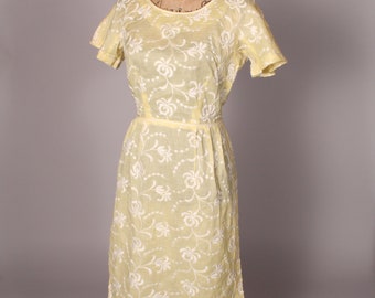 May include: A yellow vintage dress with white floral embroidery. The dress has a round neckline and short sleeves. It is fitted at the waist and flows to the knee.